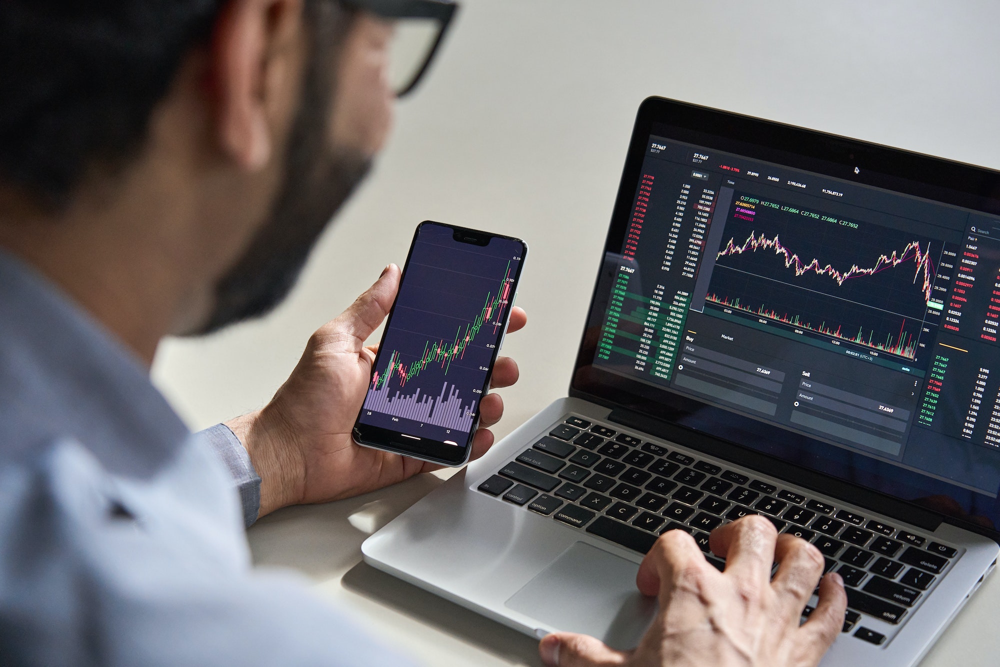 Trader checking market data on a phone and laptop